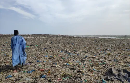 Immagine di un uomo africano che cammina su una distesa di rifiuti